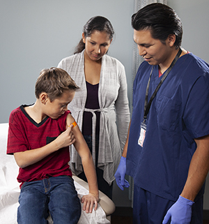 Healthcare provider giving boy injection in arm while woman looks on.